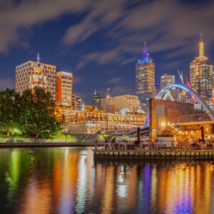 Нощна снимка на Мелбърн с отражения в реката и осветени сгради