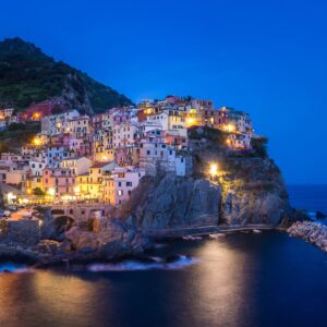 Нощна фотография на Чинкуе Тере с осветени цветни къщи по скалите.