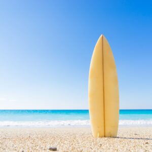 surfboard on the beach with ocean and blue sky