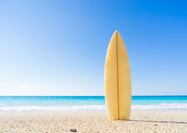 surfboard on the beach with ocean and blue sky