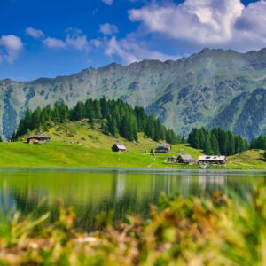 Алпийско езеро с планински хребет и къщи сред зелените склонове.