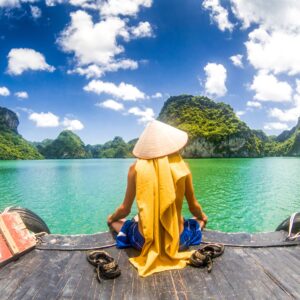 Монах на лодка гледа Халонг Бей във Виетнам.