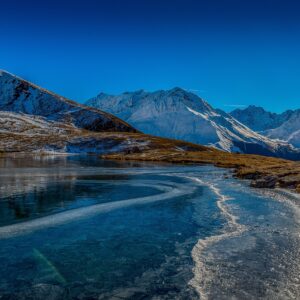 Зимно езеро с лед и заснежени планини на заден план