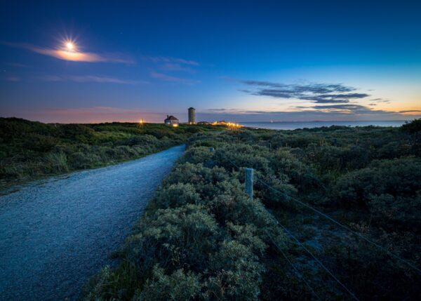 Moonlit road with lighthouse and serene night sky.