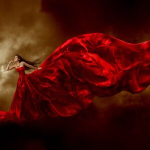 Жена в червена рокля, развята от вятъра пред облаци.