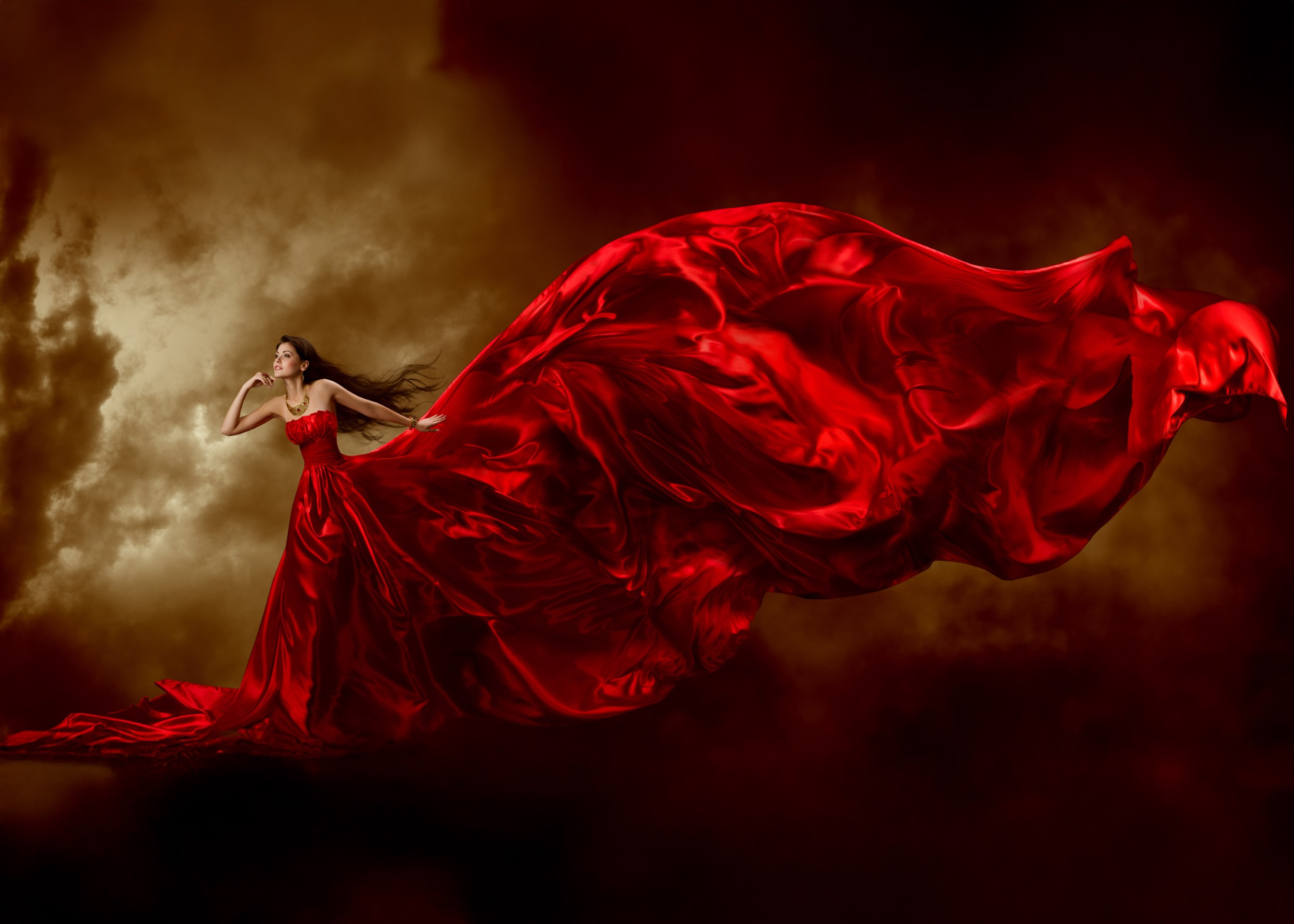 Жена в червена рокля, развята от вятъра пред облаци.