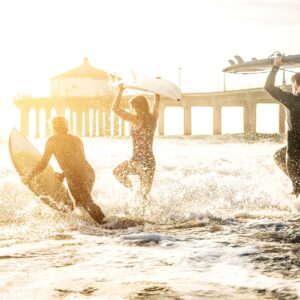 Сърфисти тичат към океана на залез със сърф дъски