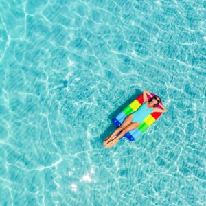 Жена върху дюшек в басейн със синя вода