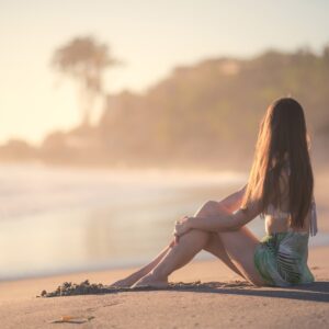 Жена седнала на плажа при залез