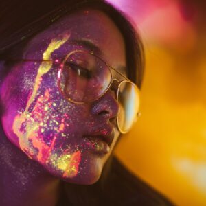 Жена с очила и цветни светлинни отражения по лицето.