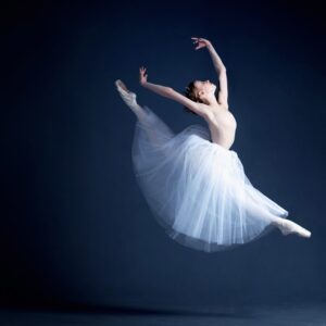 Балерина в скок с бяла пола на тъмен фон