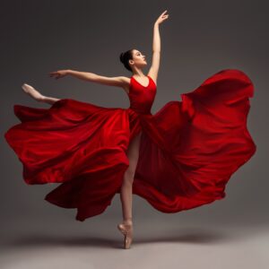 Балерина в червена рокля изпълнява скок на сцена.