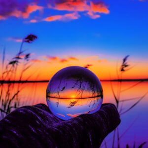 Кристална сфера с отражение на залез над езеро.