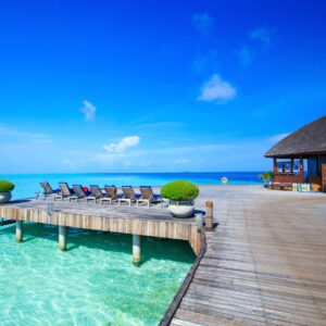 Дървен кей над тюркоазена вода с вили в далечината