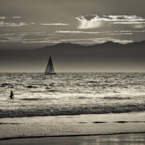 Черно-бял кадър с море и платноходка в далечината.