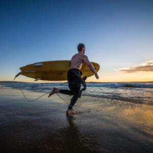 Сърфист на залез с дъска, тичащ по плажа.